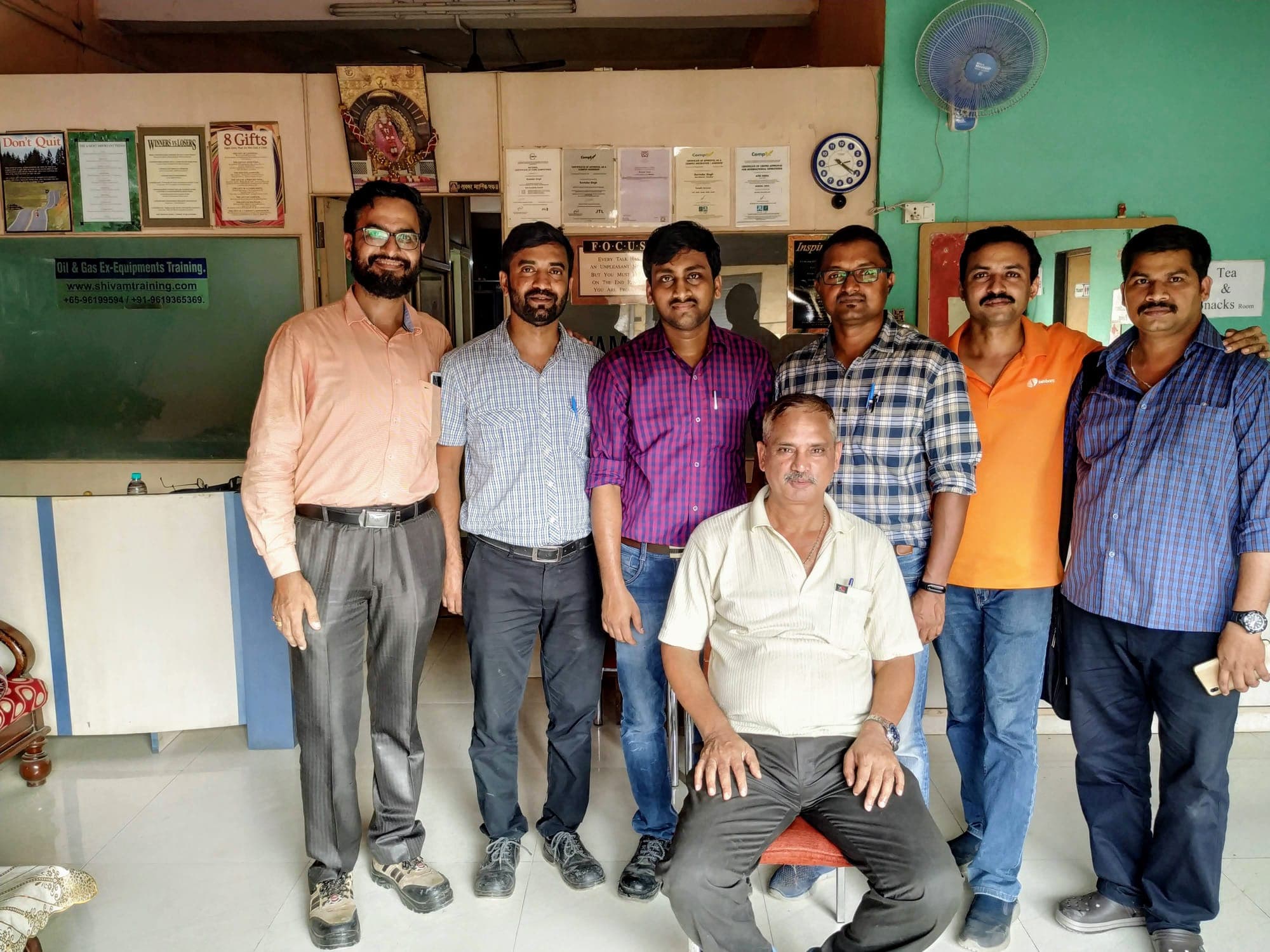 Seven engineers with their trainer in the centre's reception at the end of a course, one of them seated at the front.